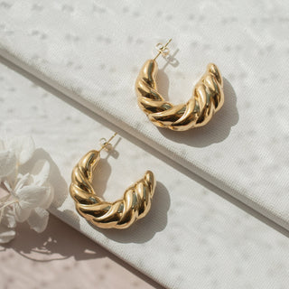 Gold hoop earrings on a textured surface with a white flower.