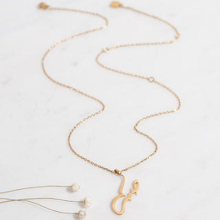 Gold Arabic "Patience" necklace with an on a white surface, alongside small white flowers.