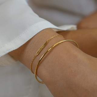 Model wearing gold islamic bracelets 'with hardship comes ease' engraved paired with plain bangle